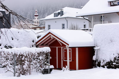 Snow covered houses by trees against sky