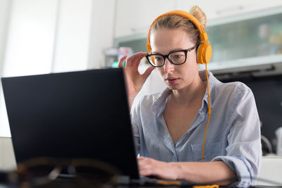 Businesswoman wearing headphones working on laptop at home