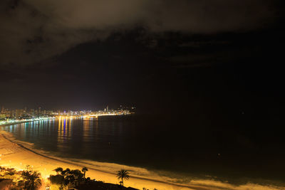 Illuminated city by sea against sky at night