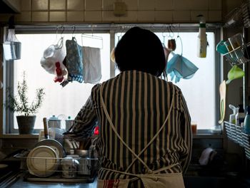 Rear view of woman standing in kitchen at home