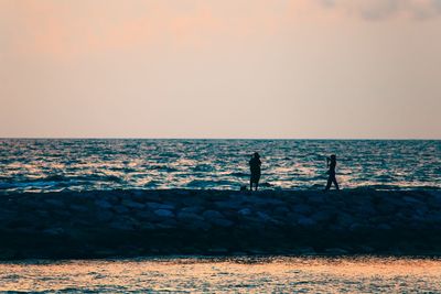 Silhouette men fishing on beach against clear sky