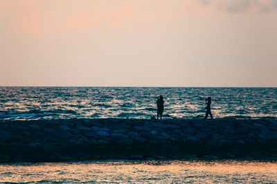 Silhouette men fishing on beach against clear sky