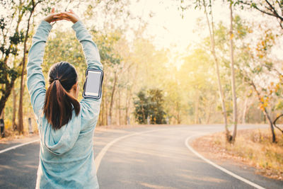 Woman exercising on road against trees