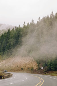 Whining mountain road with a car in a distance. road trip through the forest on foggy day