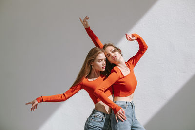Young women with arms raised dancing against wall