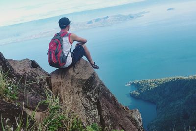 Rear view of man sitting on rock by sea
