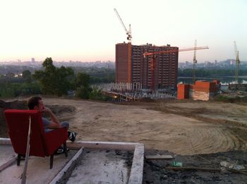Man sitting at construction site in city against sky