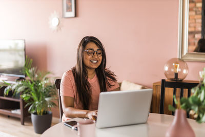 Portrait of young woman using laptop while sitting at table