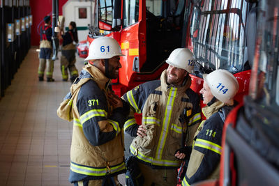 Coworkers smiling while standing against fire engine at fire station