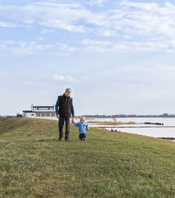 Full length of man walking with grandchild on field