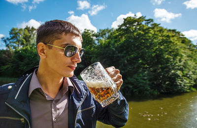 Young man wearing sunglasses drinking beer against sky