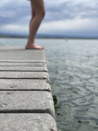 Low section of man on pier over sea against sky