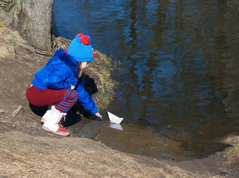 Side view of girl playing with paper boat in lake