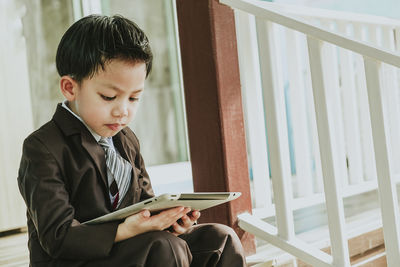 Boy looking away while sitting on window