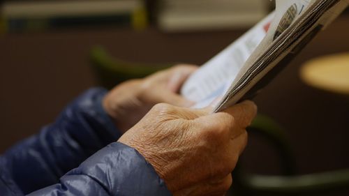 Cropped wrinkled hands of person holding newspaper