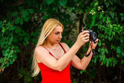 Young woman photographing while standing against plants