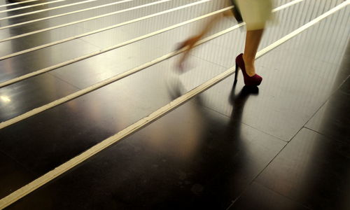 Low section of woman walking with high heels on floor