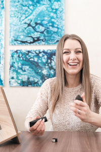 Happy laughing woman holding foundation tube and a sponge. young woman having fun with make-up. 