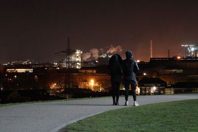 Rear view of couple standing at illuminated park against sky at night