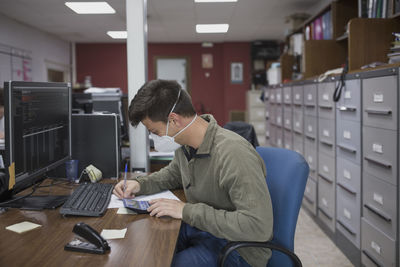 Side view of man working at the office with mask