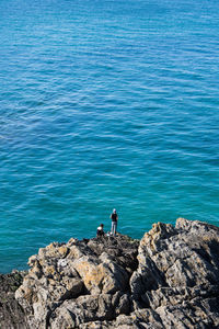 People standing on rock by sea against blue sky