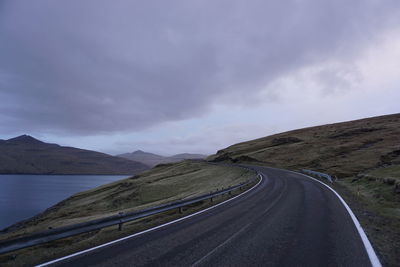 Empty road leading towards mountains against cloudy sky