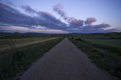 Road amidst field against sky during sunset