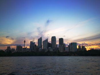 Sea by buildings against sky during sunset