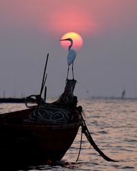 Fishing boat moored in sea against sky during sunset