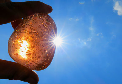 Cropped hand holding crystal stone against sky