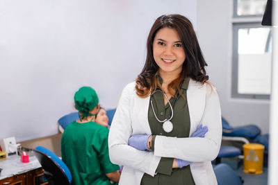 Portrait of smiling female doctor standing against wall