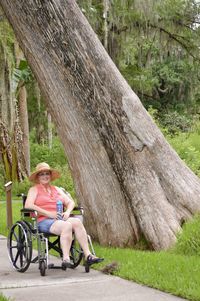 Full length of woman sitting on wheelchair by tree