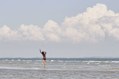 Rear view of shirtless boy jumping in sea against cloudy sky