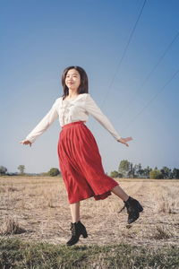 Happy young woman with arms raised on field against clear sky