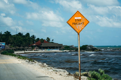 Information sign by road by sea against sky