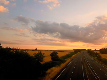 Road by trees against sky during sunset