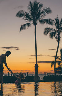 Couple in infinity pool against sky during sunset