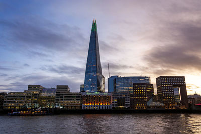 Buildings at waterfront against cloudy sky