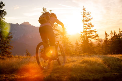 Woman riding bicycle on field against sky during sunset