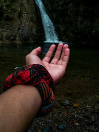 Cropped hand of man reaching waterfall
