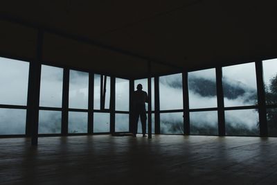 Rear view of silhouette man standing by window