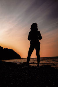 Silhouette woman standing at beach during sunset