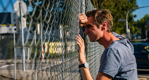 Upset man leaning head against fence. profile view.