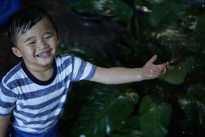 Smiling boy enjoying rainfall by plants