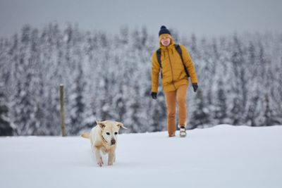 Full length of man with dog walking on snow covered land during winter