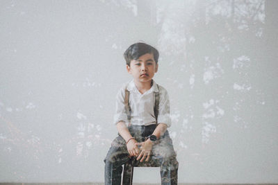 Portrait of boy sitting on stool against wall