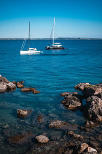 Sailboats sailing in sea against blue sky