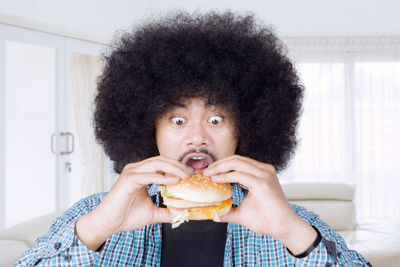 Close-up of afro man eating burger at home