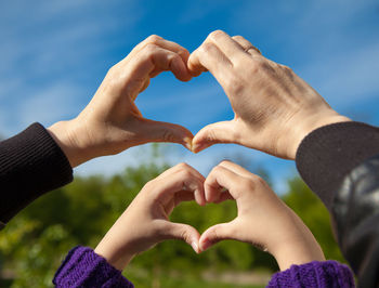 Cropped hands of mother and daughter making heart shape against sky