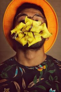 Close-up portrait of young man carrying yellow flowers in mouth